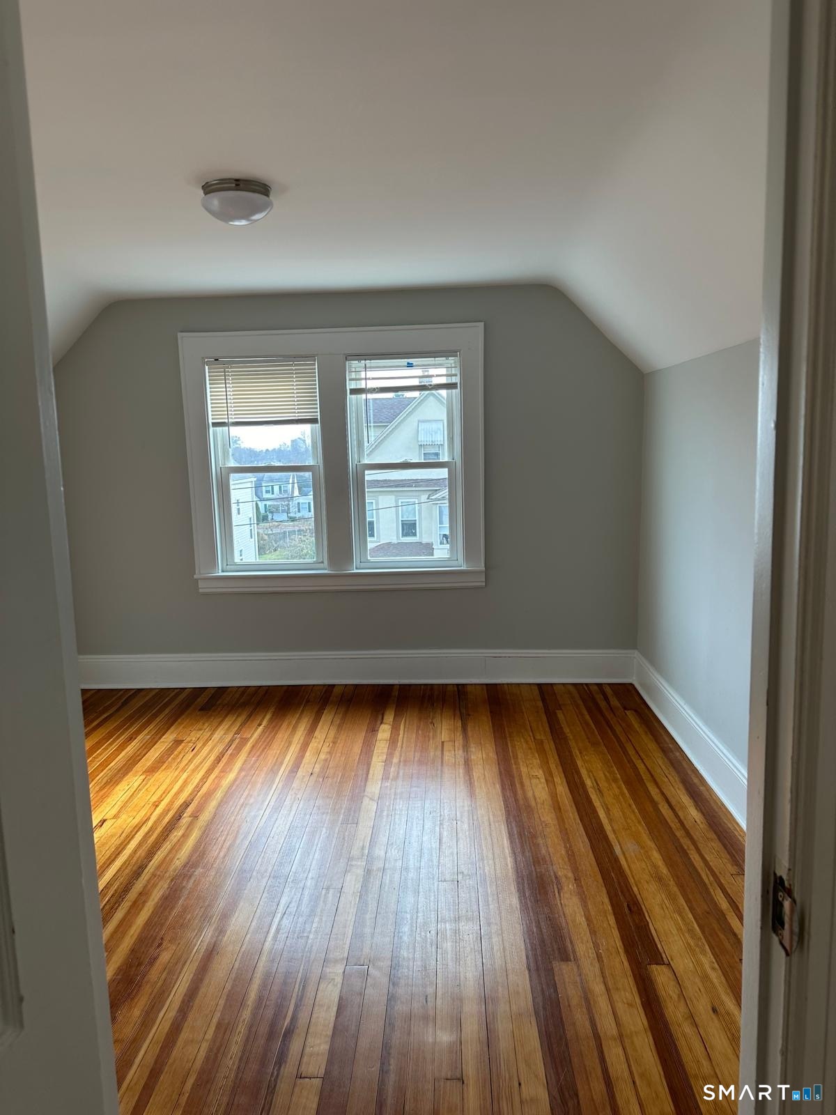Empty upstairs bedroom with a sloped ceiling, double windows, and polished hardwood floors.