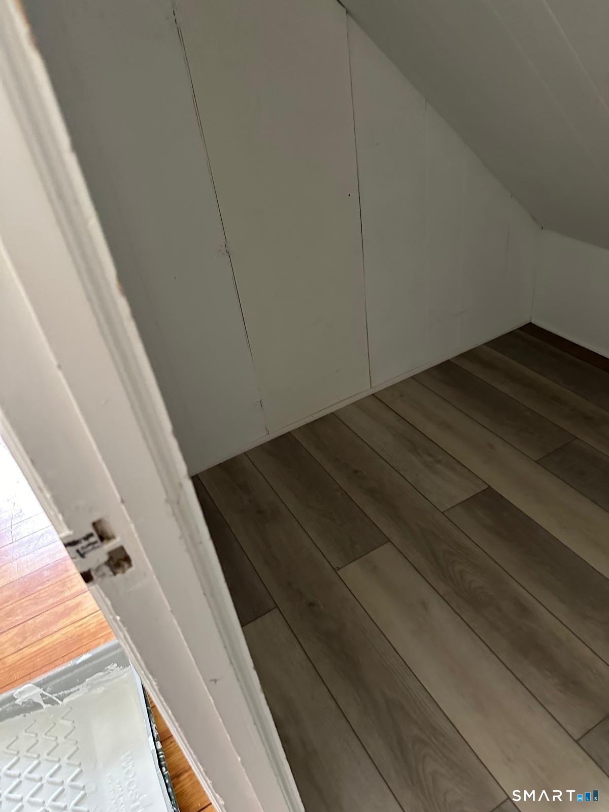 Small under-stair storage nook with white walls and gray-brown plank flooring.