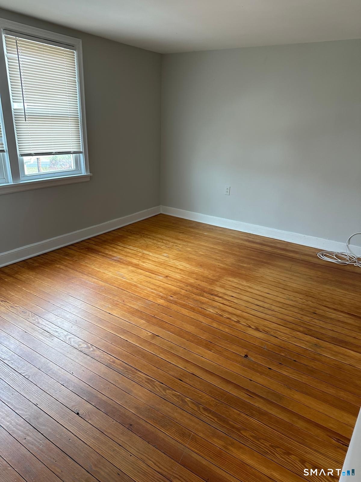 Empty room with polished hardwood floors and a window with closed blinds.