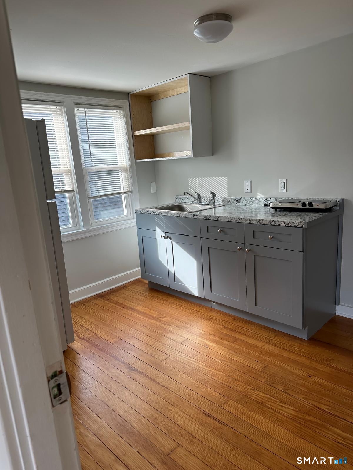 Vacant kitchen with gray cabinets, marbled counters, open shelving, and hardwood floors.