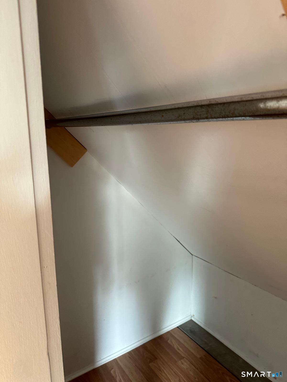 Empty under-stair closet with a metal hanging rod and wood-look flooring.