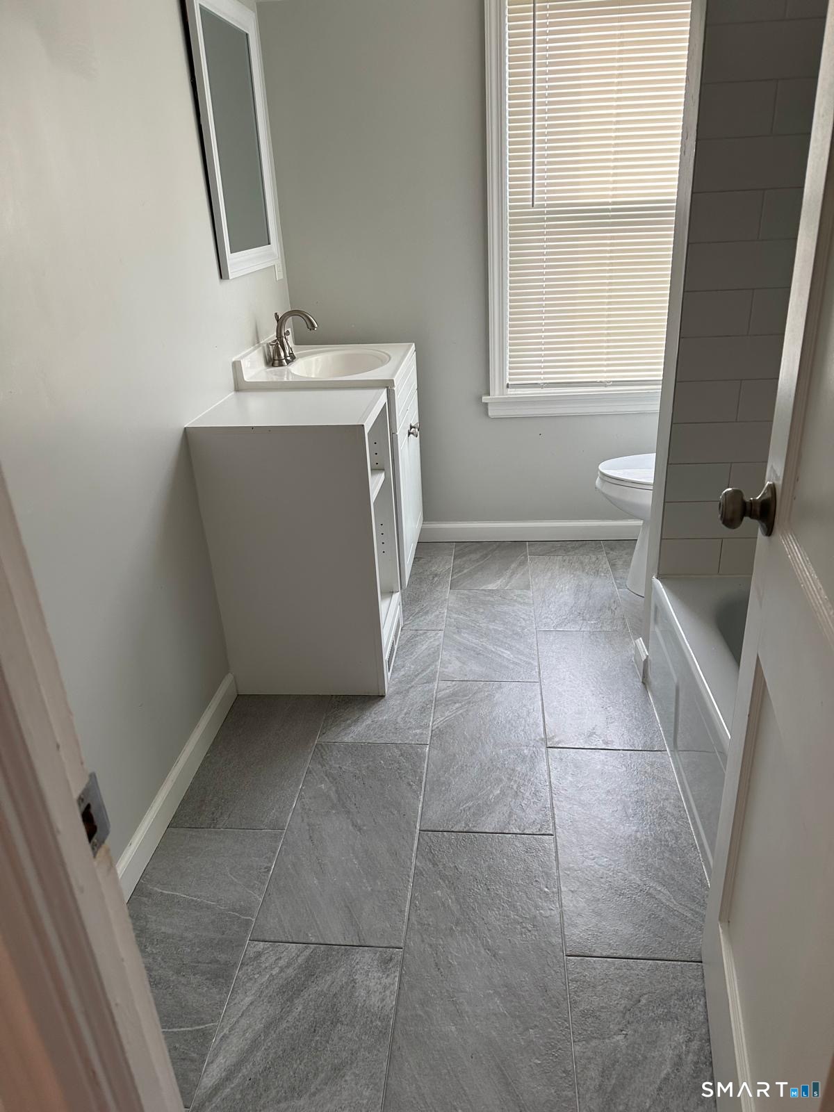 Bathroom with gray tile flooring, white vanity, and a window with closed blinds.