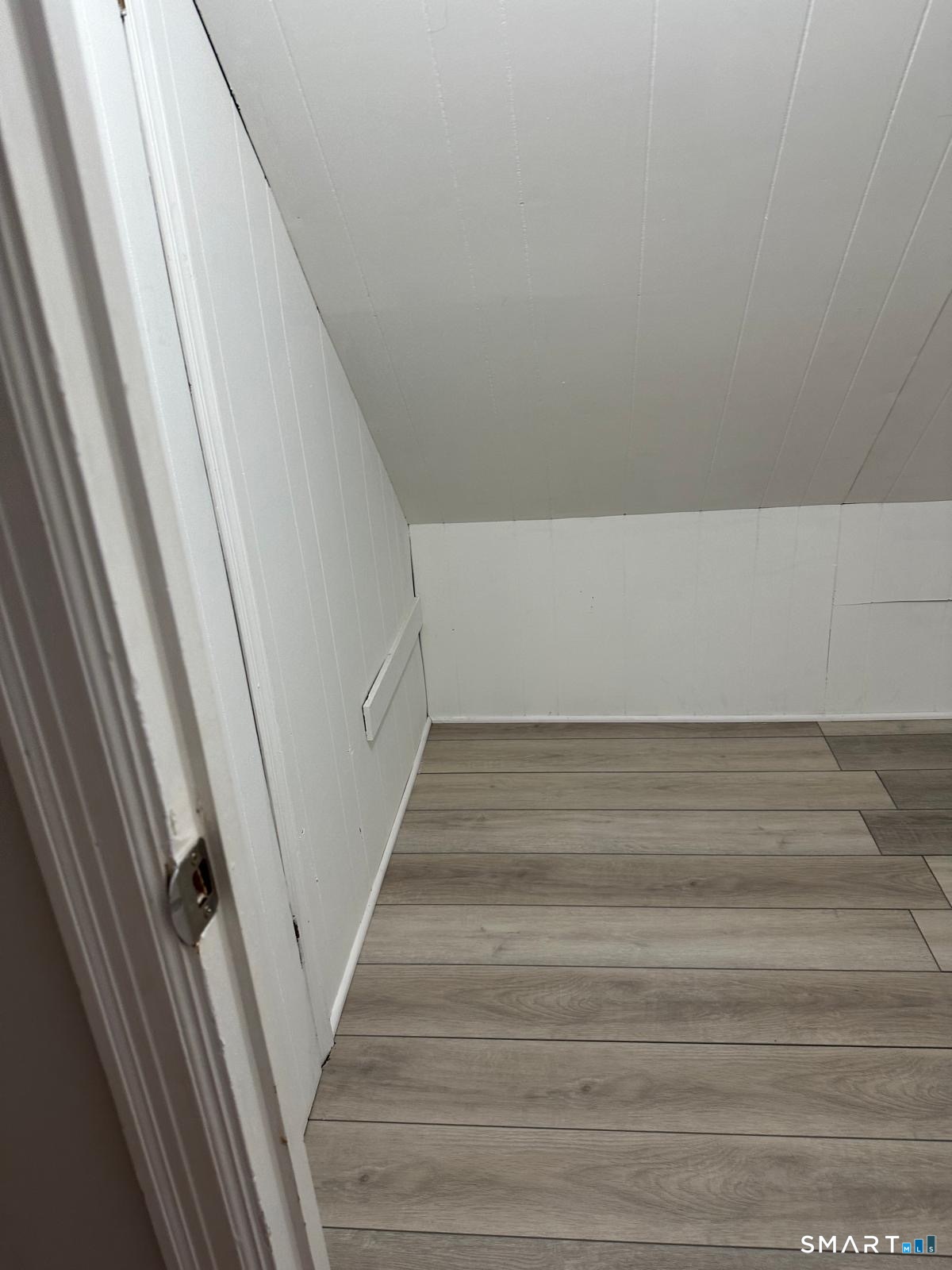 Small empty nook with a sloped white ceiling and gray plank flooring.