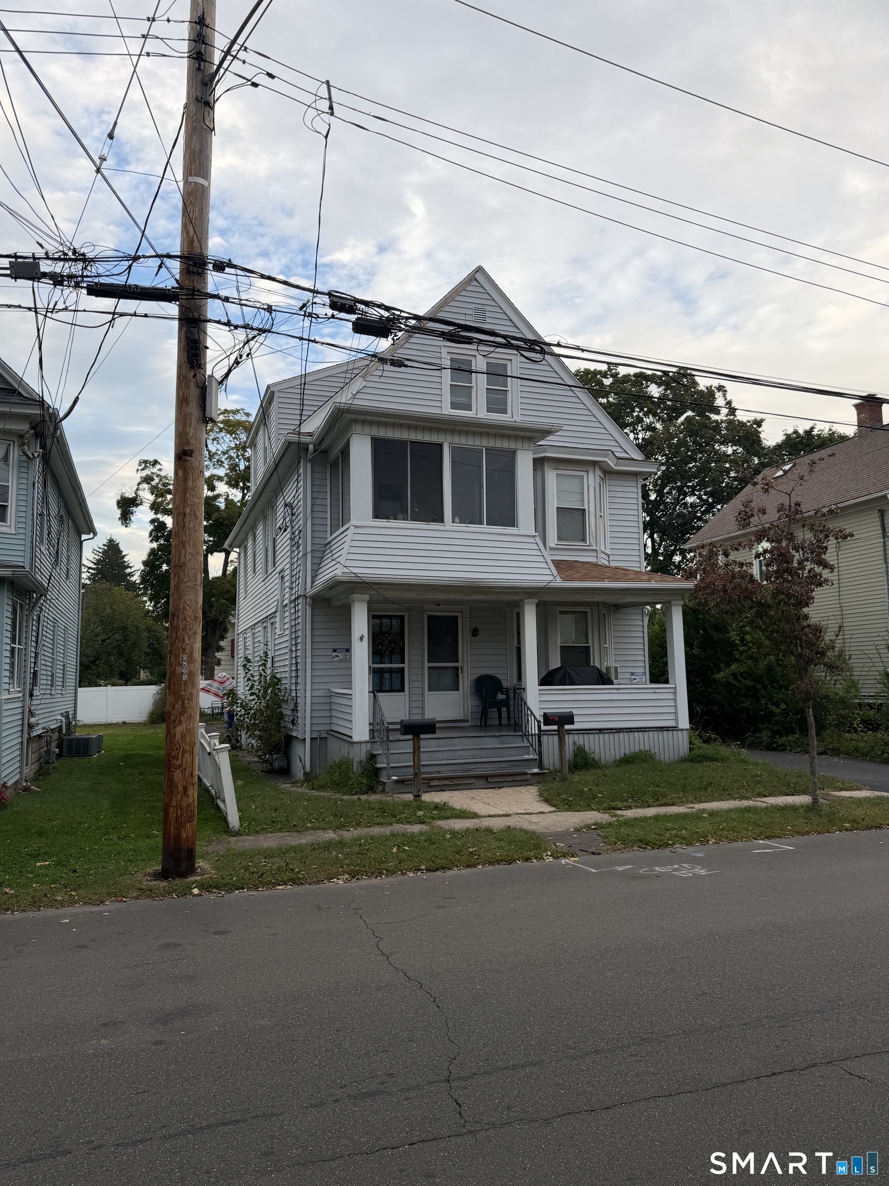 Gray multi-story house with a covered porch and steep gabled roof, viewed from across the street.