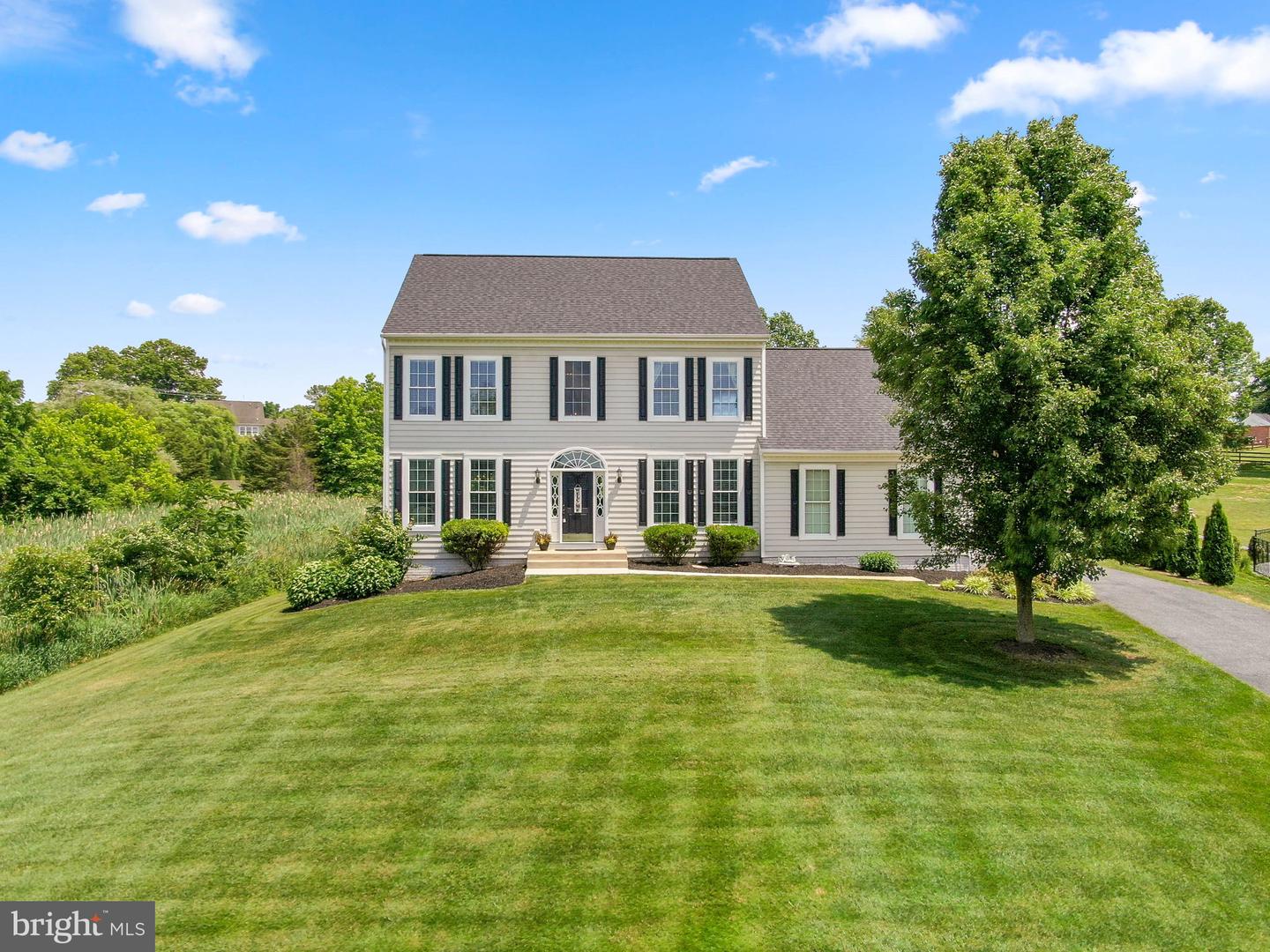 Two-story gray house with dark shutters, a broad lawn, and a large shade tree.