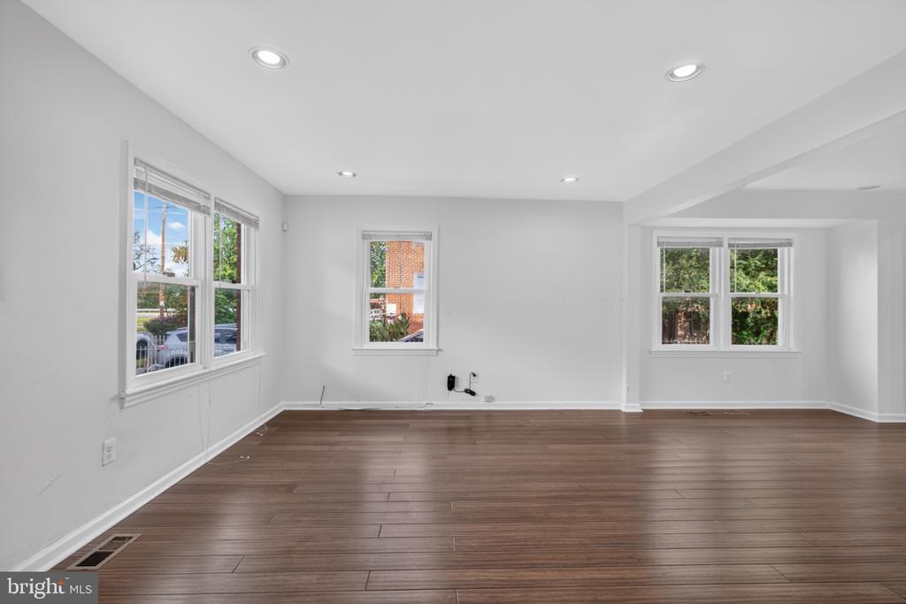 Empty living room with dark wood flooring, white walls, and multiple windows.