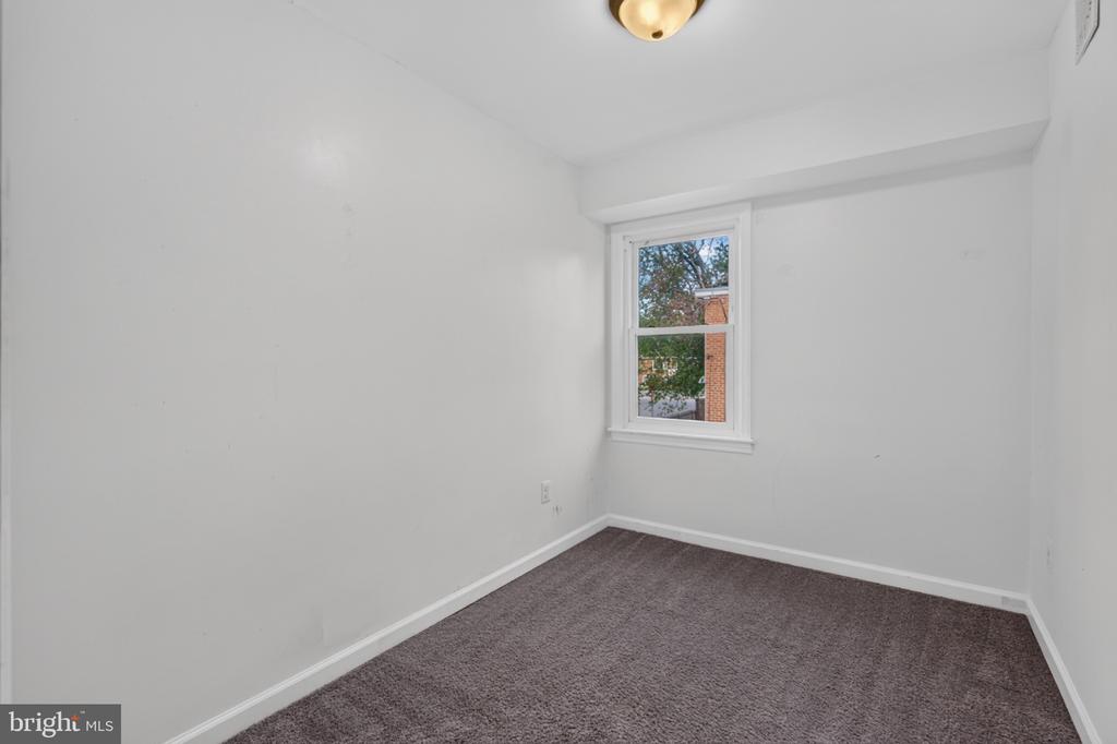 Vacant bedroom with gray-brown carpet and a single window.
