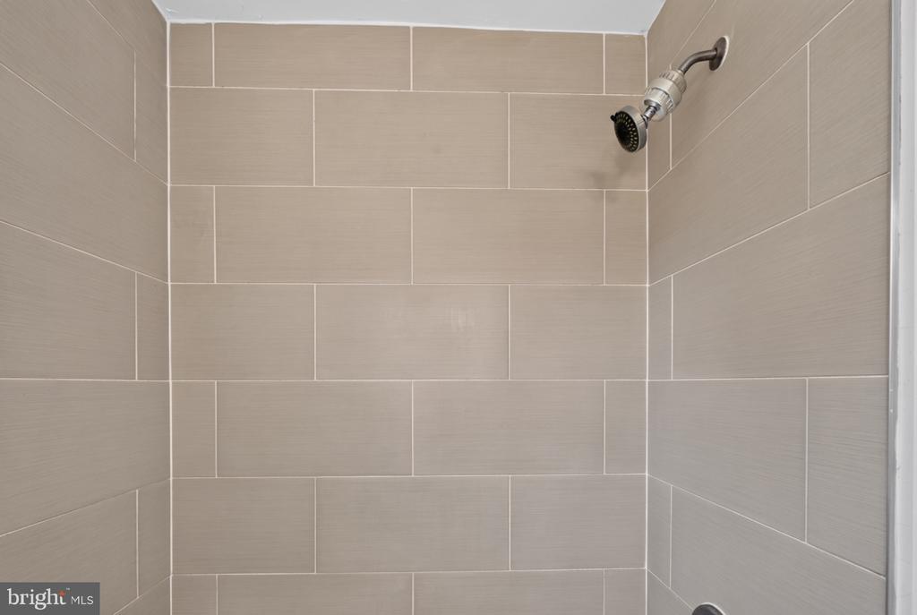 Tiled shower with large beige wall tiles and a chrome showerhead.
