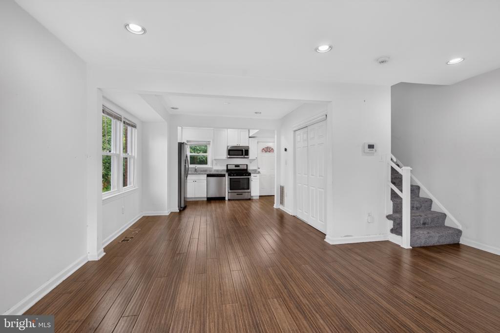 Open-plan living area with wood-look flooring, white kitchen, stainless steel appliances, and carpeted stairs.