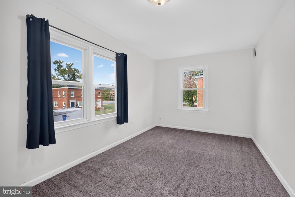 Empty bedroom with gray-brown carpet, dark curtains, and three windows.