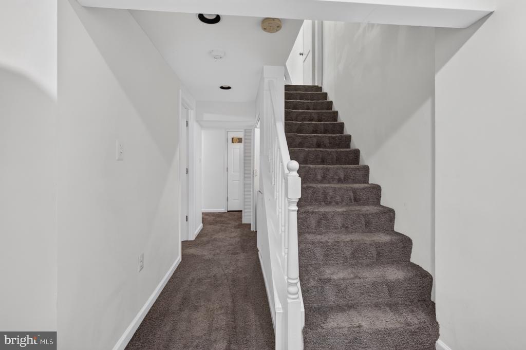 Carpeted staircase beside a narrow hallway with white walls and railing.