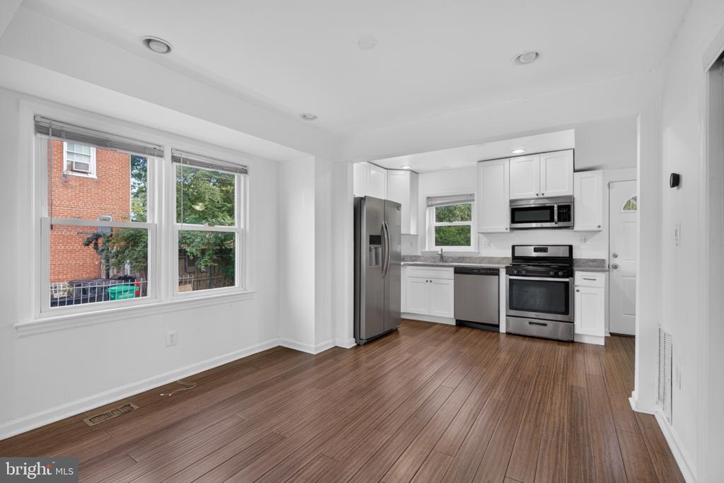 Bright kitchen with white cabinets, stainless appliances, and an adjoining empty dining area.