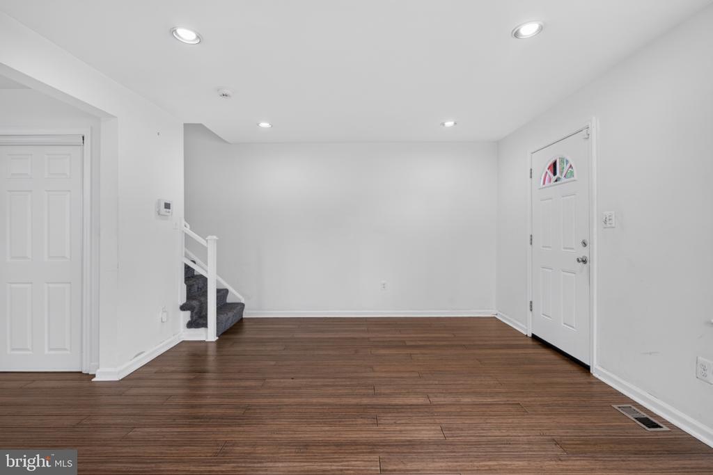 Empty room with brown plank flooring, recessed lights, a carpeted staircase, and two white doors.