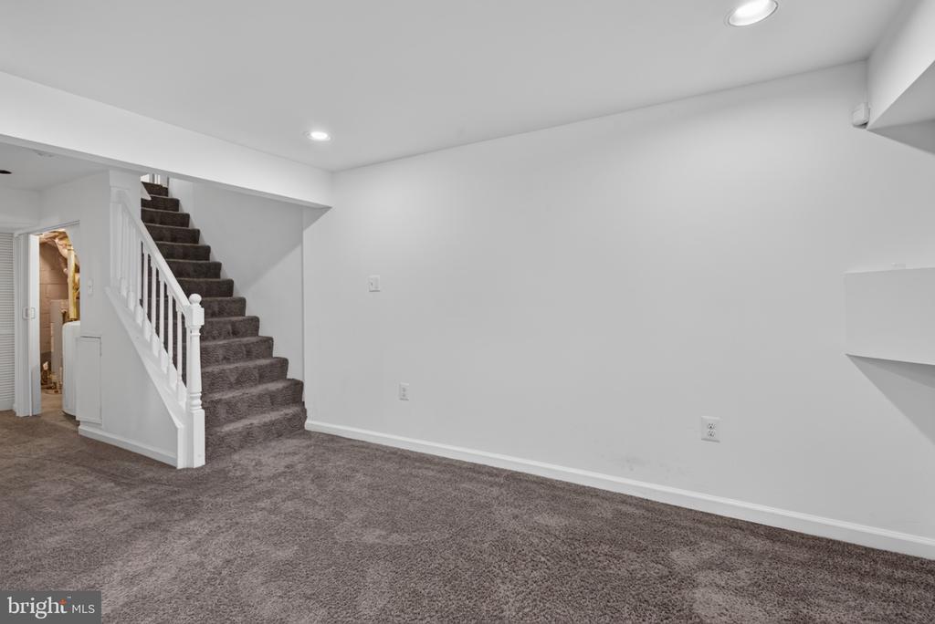 Finished basement room with gray carpet and a carpeted staircase with white railing.