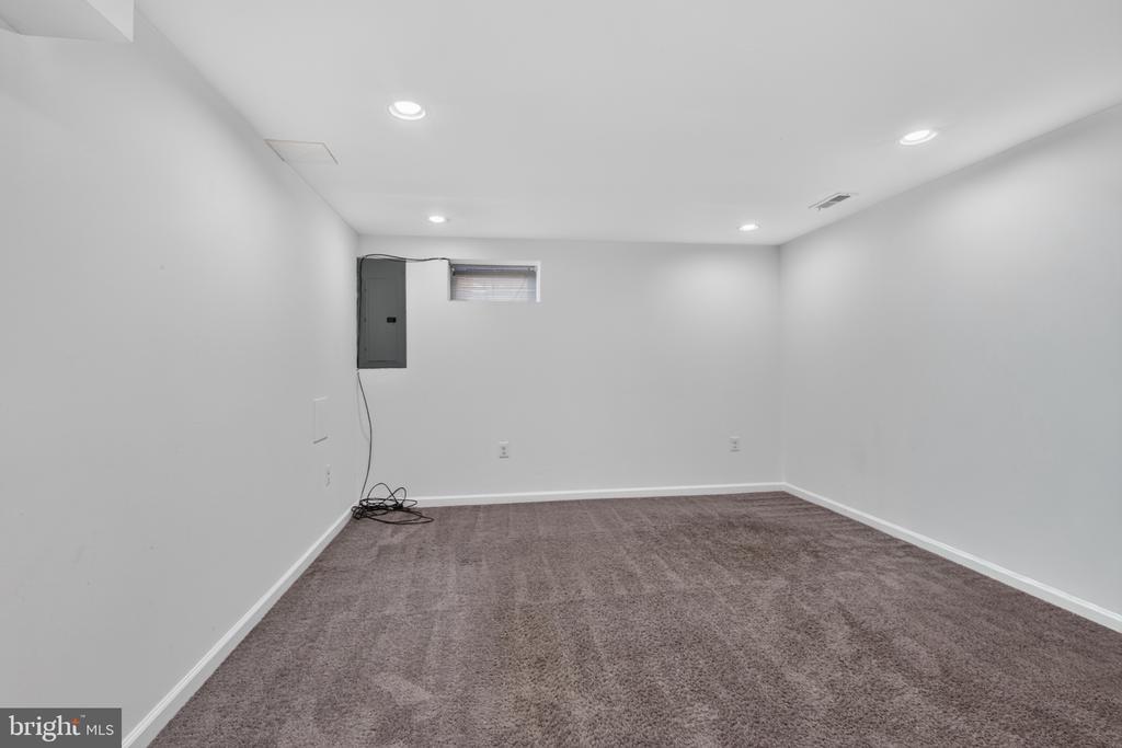 Empty carpeted room with recessed lights, a small high window, and an electrical panel.