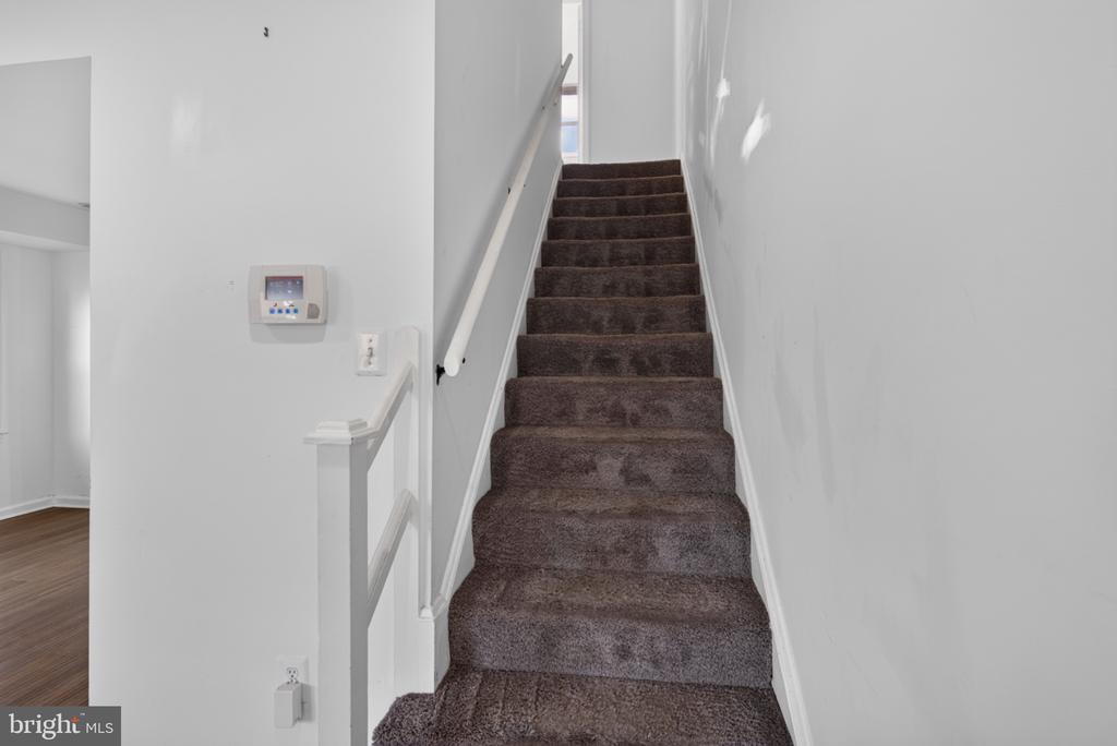 Carpeted staircase with a white handrail and thermostat on the wall.