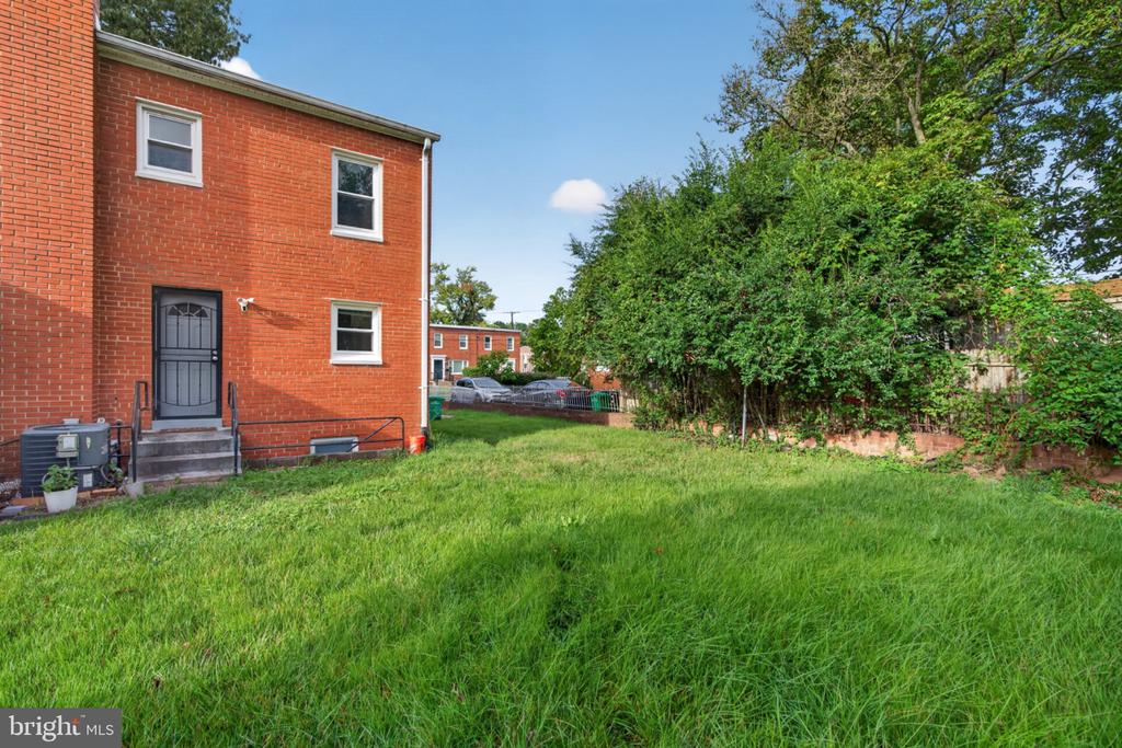 Red-brick home beside a broad grassy yard bordered by mature trees and shrubs.
