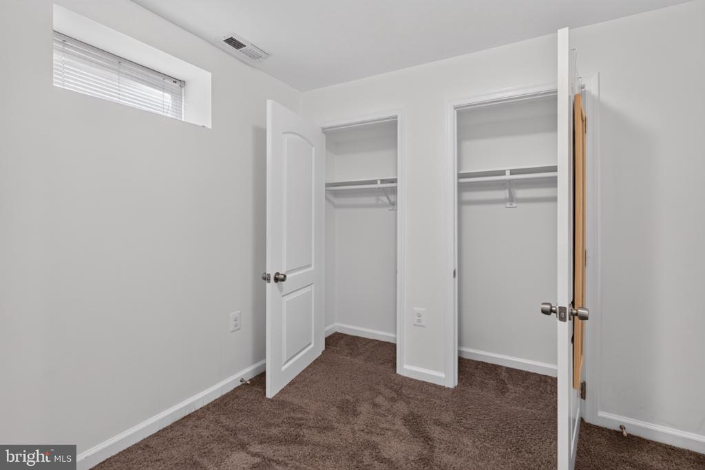 Empty carpeted bedroom with two open closets and a high window with blinds.