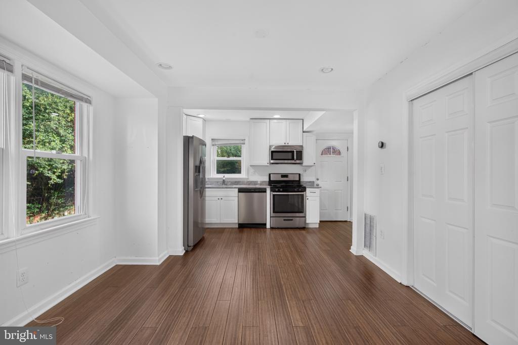 Unfurnished dining area opening to a white kitchen with stainless steel appliances and wood-look floors.
