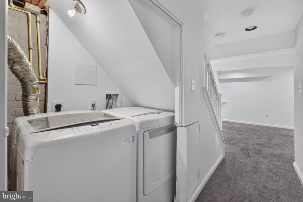 Laundry area with a white washer and dryer beside a carpeted lower-level room.
