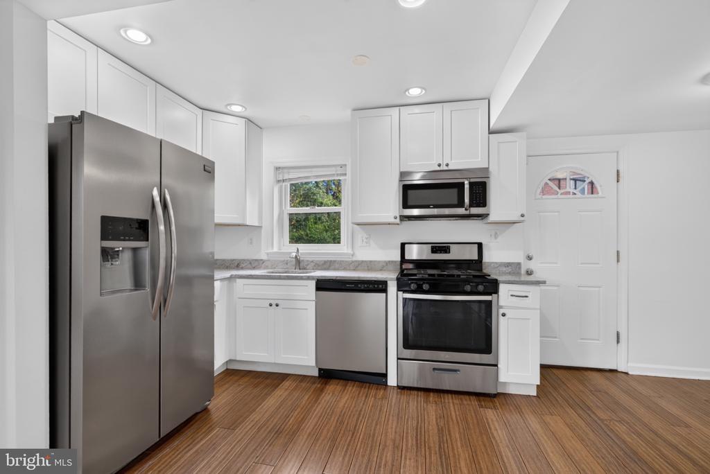 Kitchen with white cabinets, stainless steel appliances, and warm wood flooring.