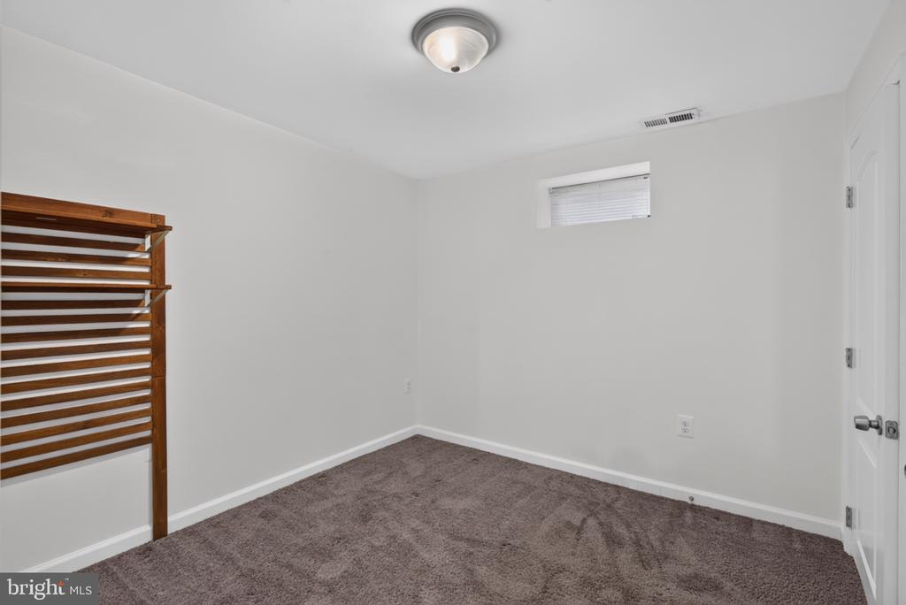 Empty bedroom with carpet, a high window, and wooden slatted built-in shelving.