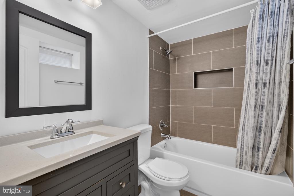 Bathroom with a dark vanity, large black-framed mirror, and tiled tub-shower.