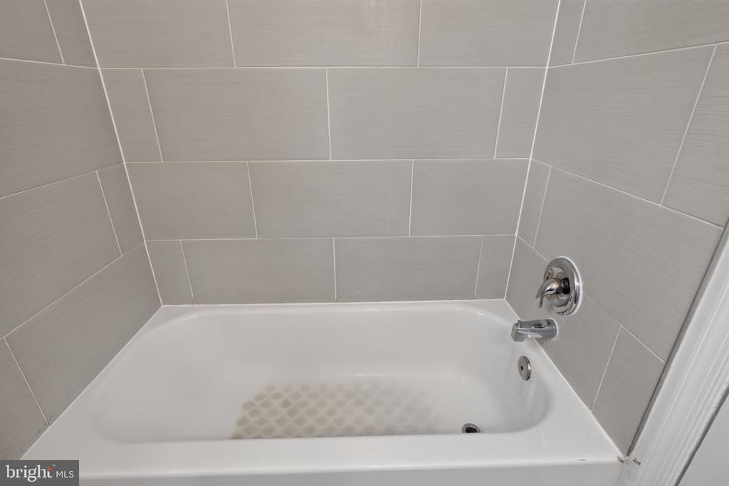 White bathtub with chrome fixtures and a large light gray tiled surround.