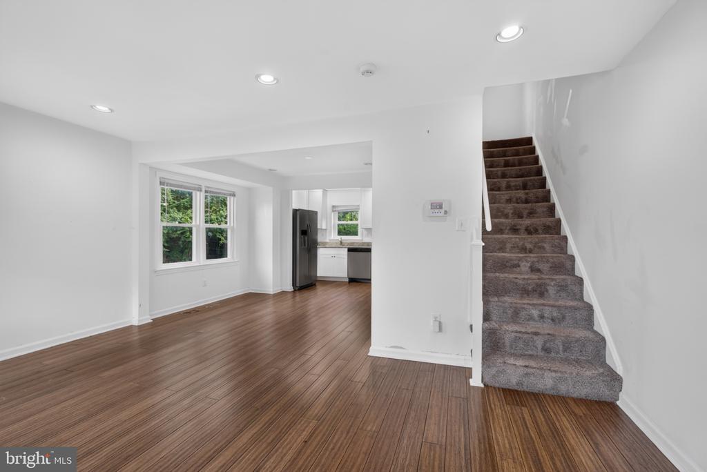 Open living area with wood-look flooring, adjoining kitchen, and carpeted staircase.
