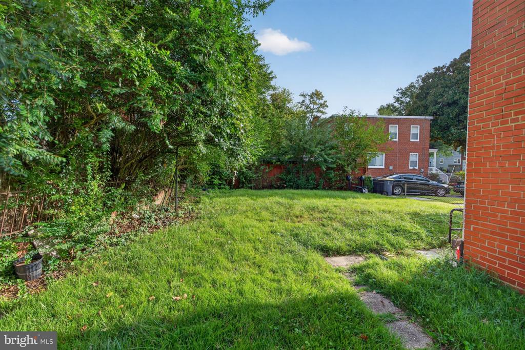 Grassy side yard with mature trees, a concrete path, and a red brick house.