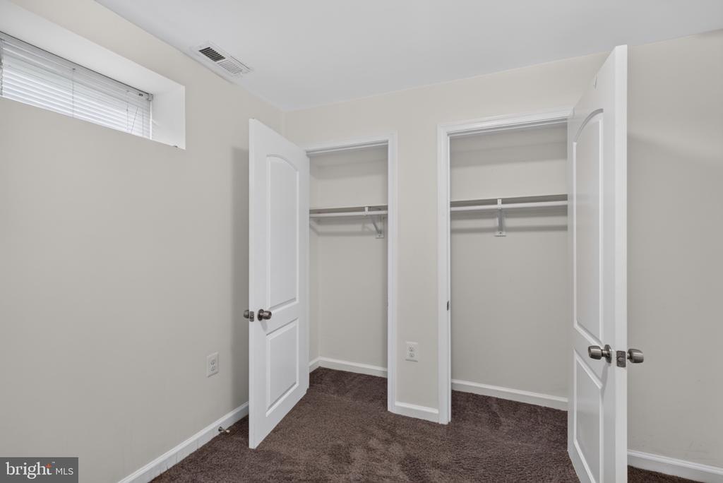 Empty carpeted room with two open closets and a high window with blinds.