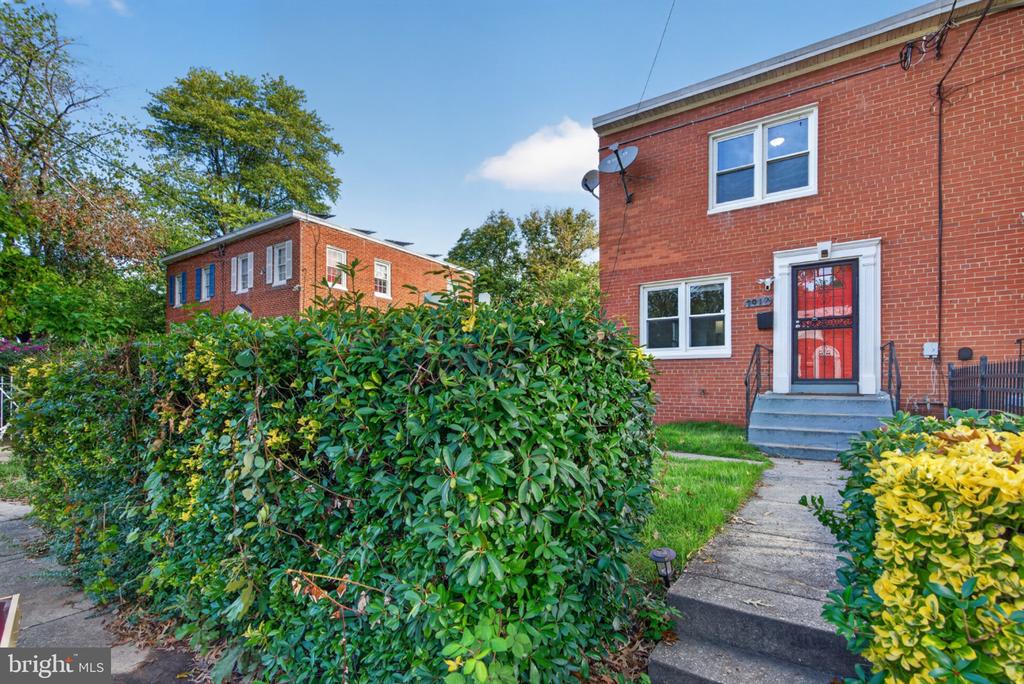 Red-brick home with a red front door, concrete steps, and shrubs along the walkway.
