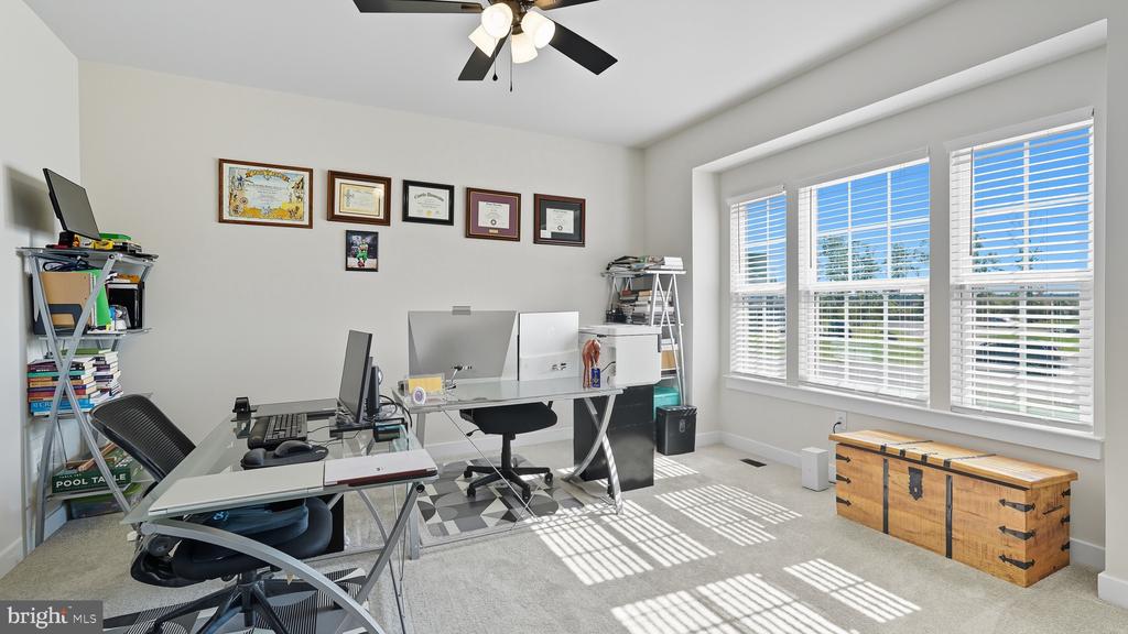 Home office with multiple desks, computer monitors, and large windows with white blinds.