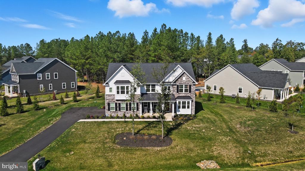 Aerial view of a two-story home with white siding, stone accents, and a broad front lawn.