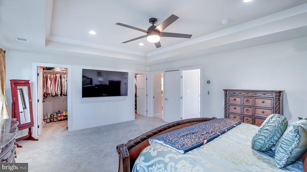 Furnished bedroom with a tray ceiling, ceiling fan, wall-mounted television, and open walk-in closet.