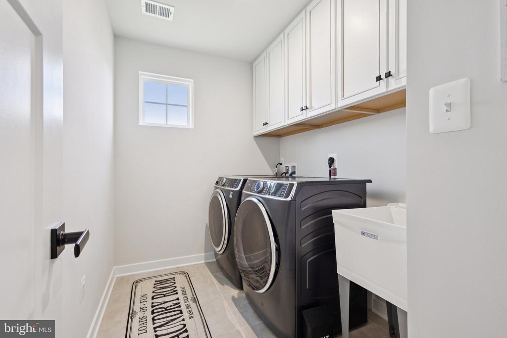 Laundry room with dark front-loading washer and dryer, white cabinets, and a utility sink.