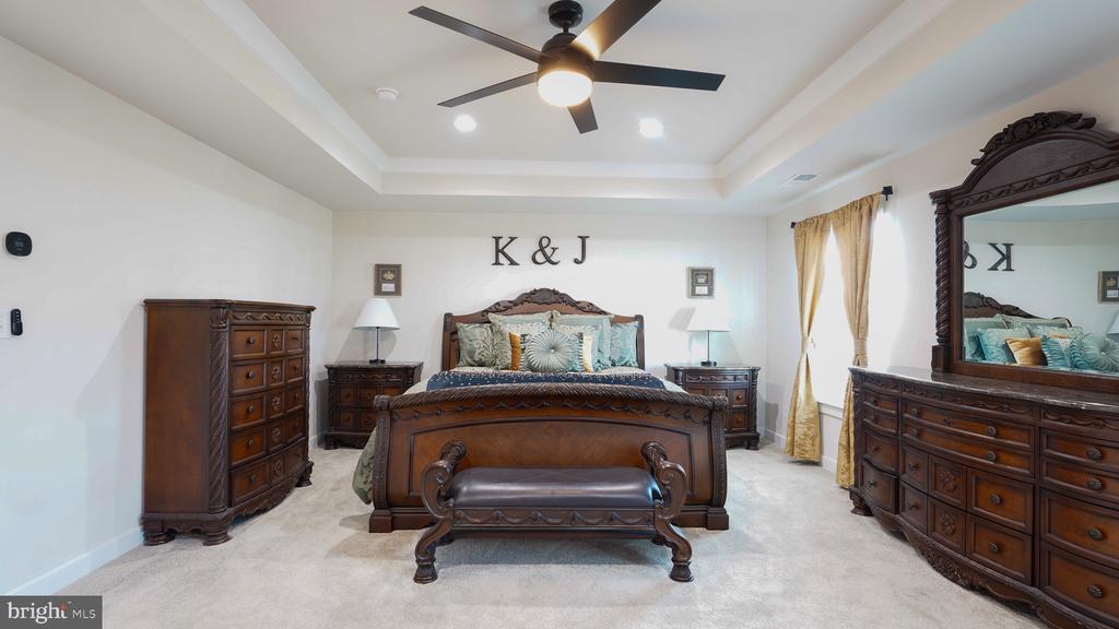 Bedroom with ornate dark wood furniture, a tray ceiling, ceiling fan, and light carpet.