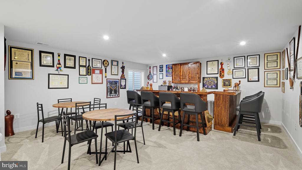 Recreation room with a wooden bar, two round tables, and walls covered in framed certificates and memorabilia.