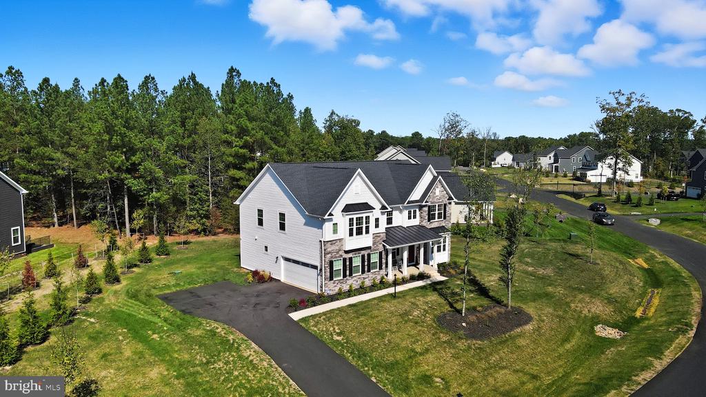 Aerial view of a two-story white house with stone accents, driveway, and wooded surroundings.