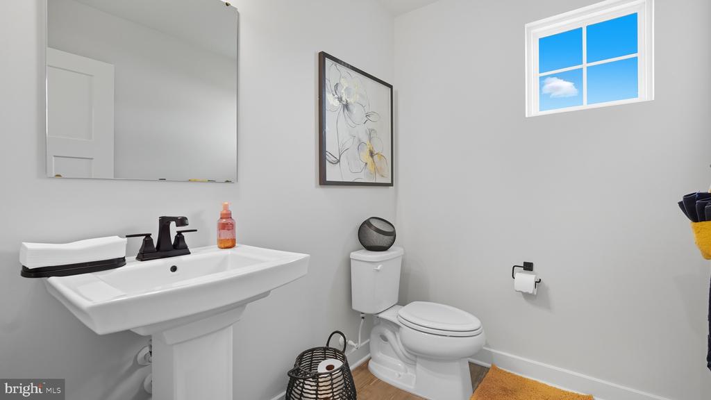Bathroom with a white pedestal sink, toilet, framed floral artwork, and a high window.