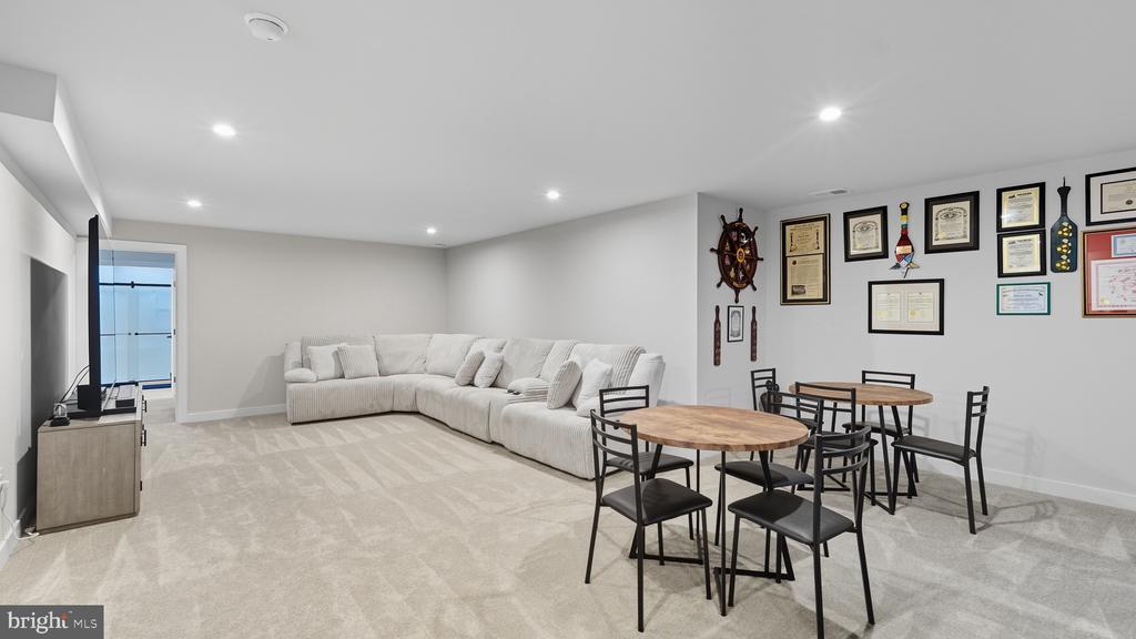 Living and dining area with a white sectional, two round tables, and framed certificates.