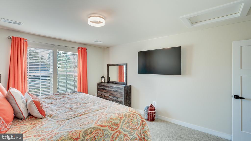 Furnished bedroom with coral curtains, a patterned bedspread, and a wall-mounted television.