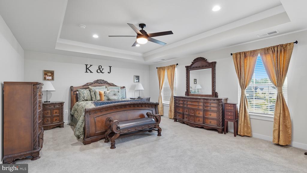 Furnished bedroom with a carved wooden bed, matching dresser, gold curtains, and tray ceiling.