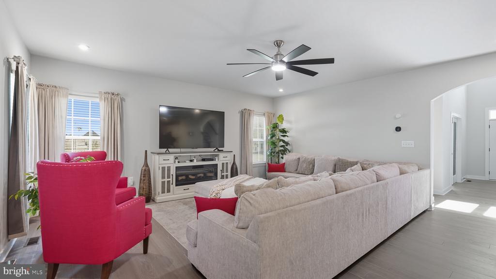 Living room with a large sectional, bright pink armchairs, and a TV above a fireplace.