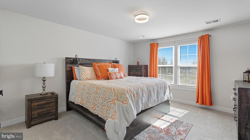Bedroom with a dark wood bed, orange patterned bedding, and bright orange curtains beside a sunlit window.