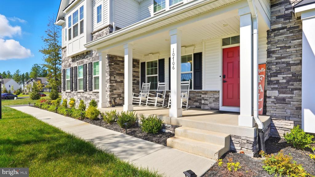 House front with stone veneer, covered porch, white rocking chairs, and a bright red door.