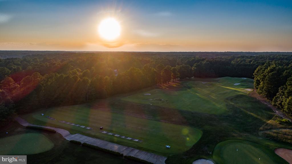 Aerial view of a golf course at sunset, with wooded fairways and putting greens.