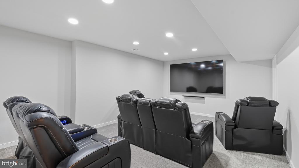 Furnished home theater with black leather recliners facing a large wall-mounted television.