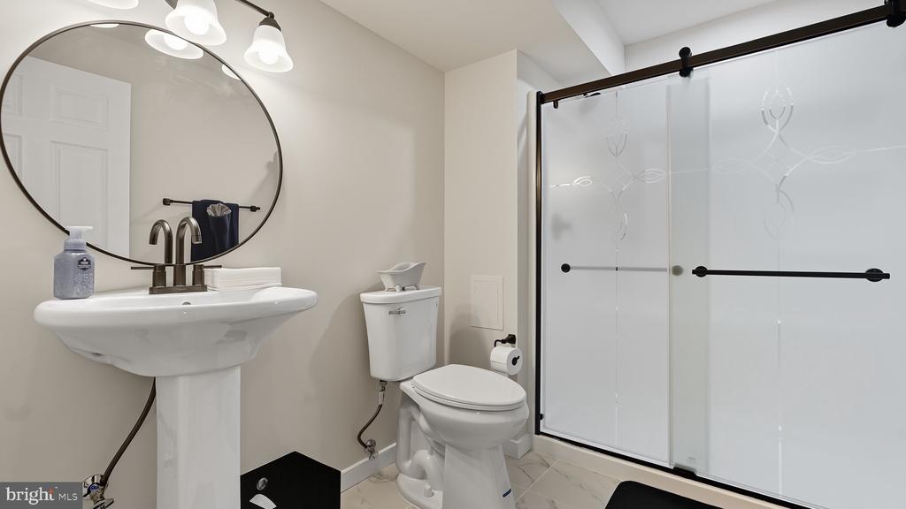 Bathroom with pedestal sink, oval mirror, toilet, and glass-enclosed shower.
