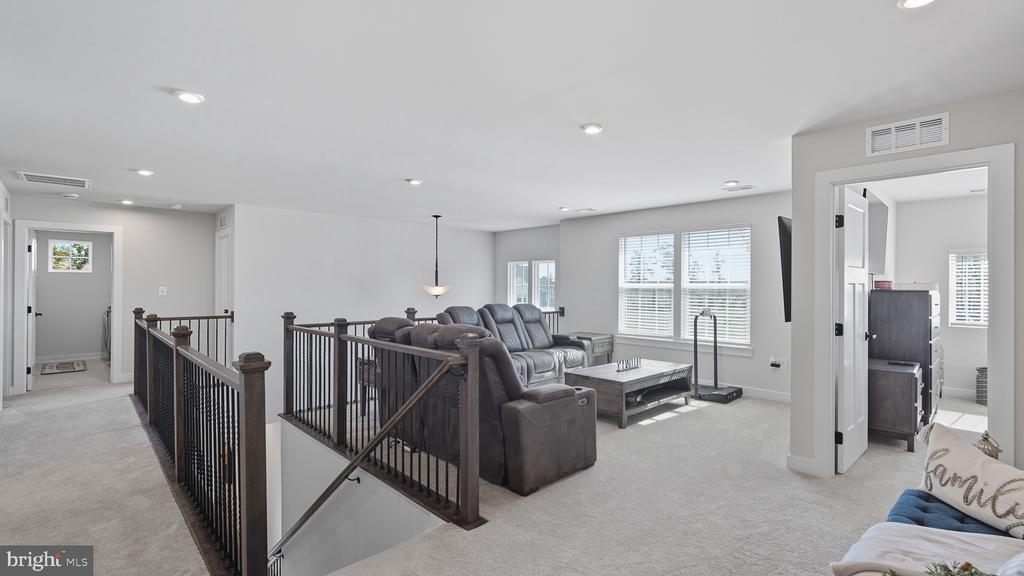Upstairs living area with a gray sectional, carpeted floor, and dark stairwell railing.